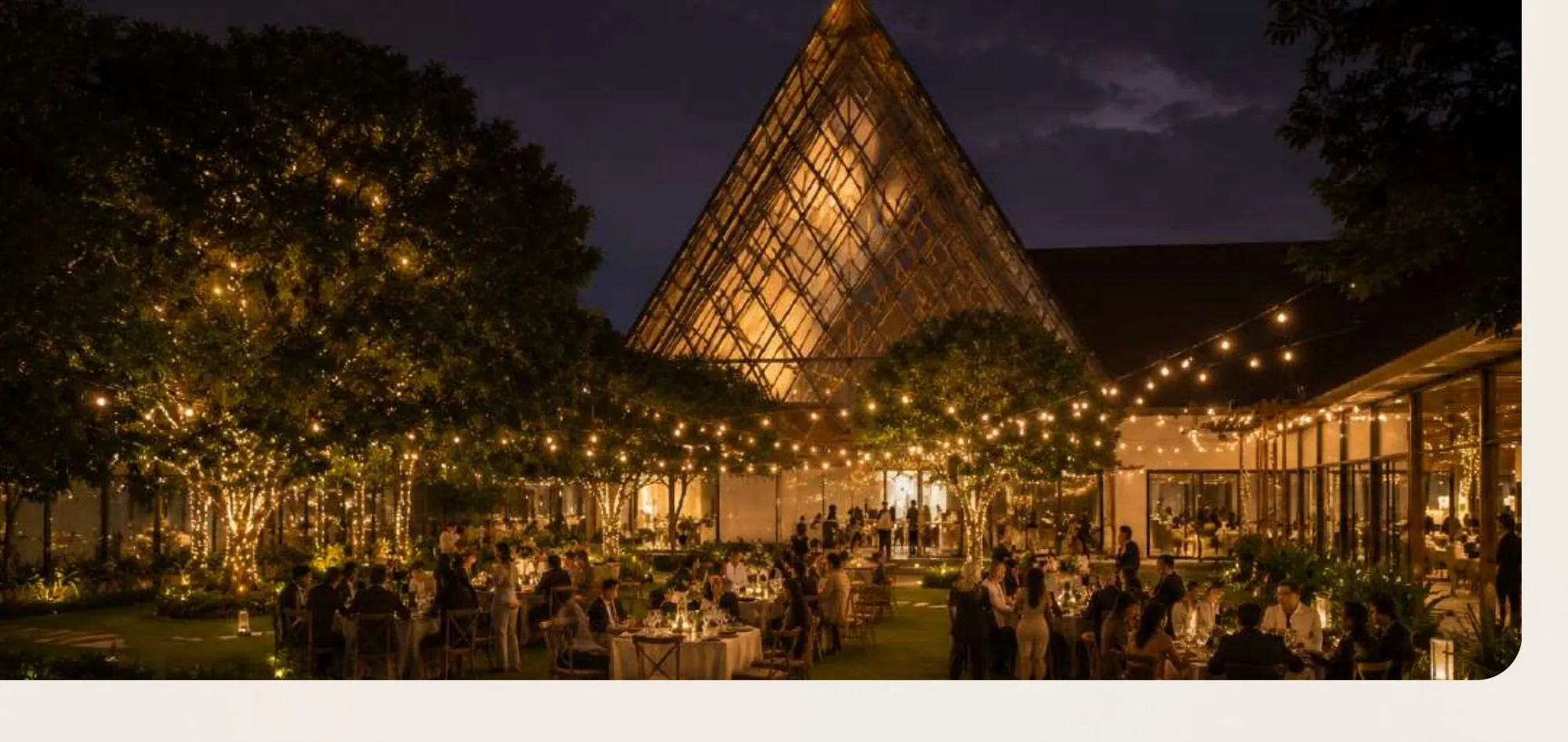 The venue at night, strung with lights, guests seated under the trees